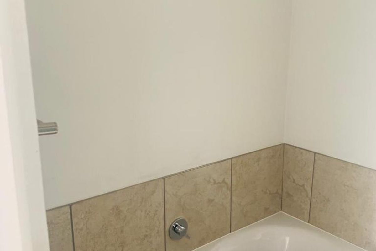 A clean bathroom featuring a built-in bathtub with neutral-toned tiled splashback and chrome fixtures.