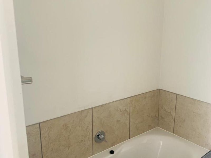 A clean bathroom featuring a built-in bathtub with neutral-toned tiled splashback and chrome fixtures.