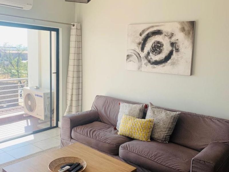 A well-maintained living room featuring tiled flooring, a wall-mounted air conditioning unit, and a large sliding glass door leading to an outdoor balcony.