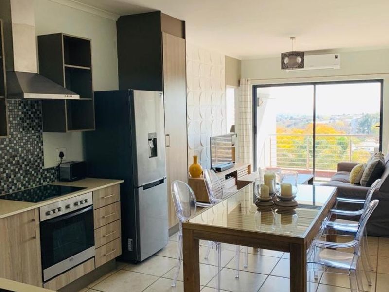 Open-plan living and kitchen area featuring modern cabinetry, mosaic backsplash, tiled flooring, and a sliding door leading to a balcony with scenic views.