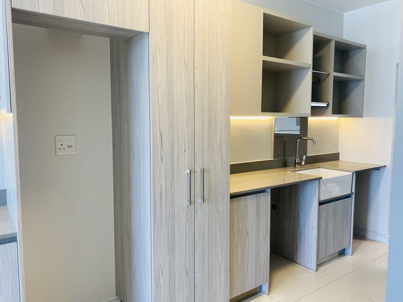 Modern kitchen featuring light wood-grain cabinetry, stone countertops, an apron-front sink, and integrated under-cabinet lighting in a clean, contemporary finish.
