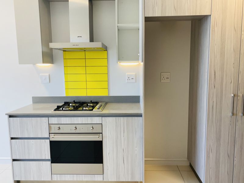 Modern kitchen featuring light wood-grain cabinetry, stone countertops, a gas hob, electric oven, and a vibrant yellow tiled splashback.