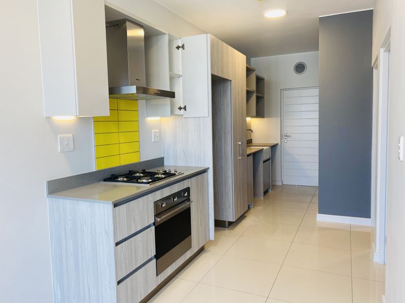 Modern kitchen featuring light wood-grain cabinetry, stone countertops, a gas hob, electric oven, and a vibrant yellow tiled backsplash.