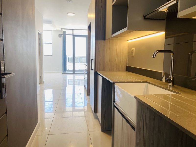 Modern kitchen featuring sleek built-in cabinetry, stone countertops, and a stylish apron-front sink, leading into an open-plan living area with balcony access.