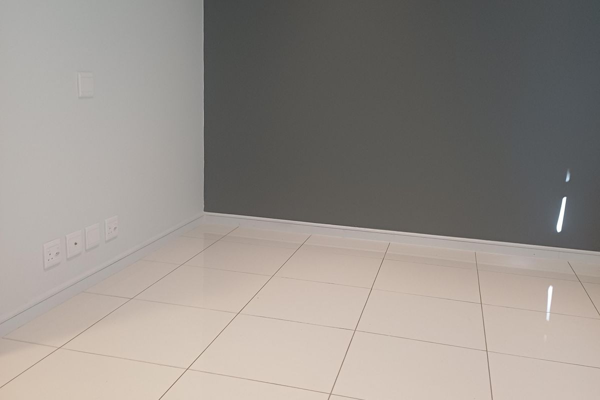 A bright, empty living area featuring modern white floor tiles and a contrasting grey feature wall, ready for personalization.
