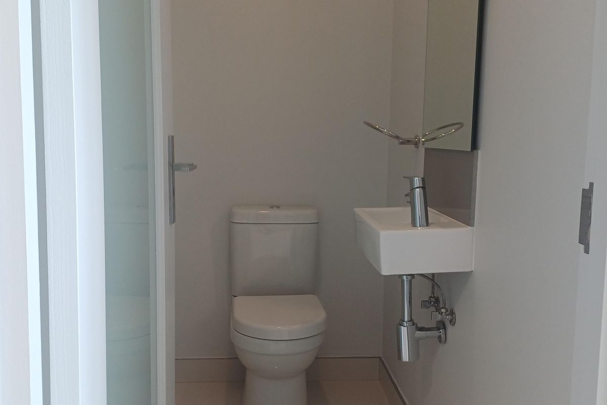 A clean and modern guest bathroom featuring a wall-mounted basin, chrome fixtures, and a neutral tiled floor.