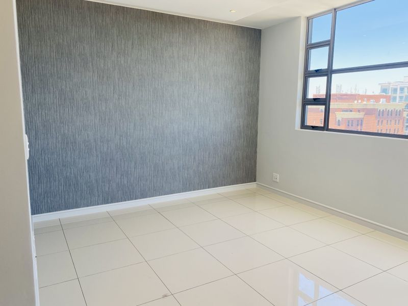 A bright, empty bedroom featuring large tiled floors, a modern textured feature wall, and an aluminium-framed window with urban views.