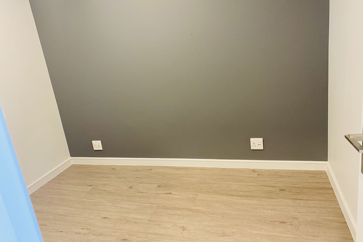 A clean, empty bedroom featuring modern laminate flooring and a neutral grey accent wall with integrated electrical sockets.