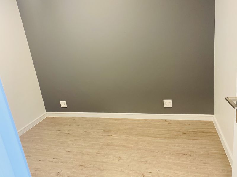 A clean, empty bedroom featuring modern laminate flooring and a neutral grey accent wall with integrated electrical sockets.