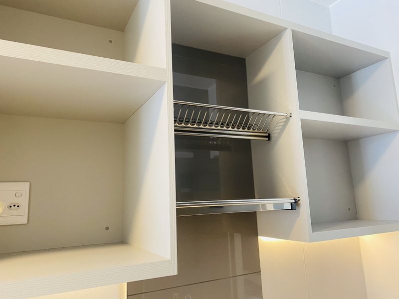 Close-up view of modern kitchen cabinetry featuring built-in shelving, an integrated dish drying rack, and subtle under-cabinet lighting.