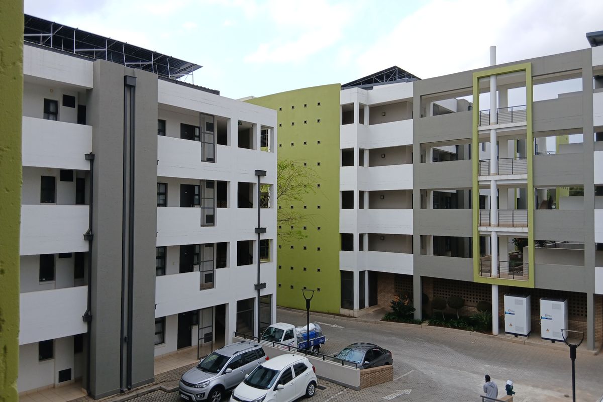 A view of a modern multi-story apartment complex featuring paved parking areas, external stairwells, and balconies with contemporary architectural finishes.