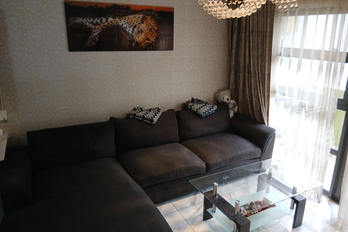 A comfortable living room featuring tiled flooring, a decorative crystal chandelier, and a sliding glass door providing access to the balcony.