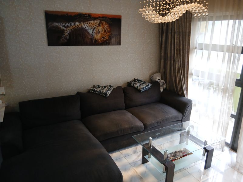 A comfortable living room featuring tiled flooring, a decorative crystal chandelier, and a sliding glass door providing access to the balcony.