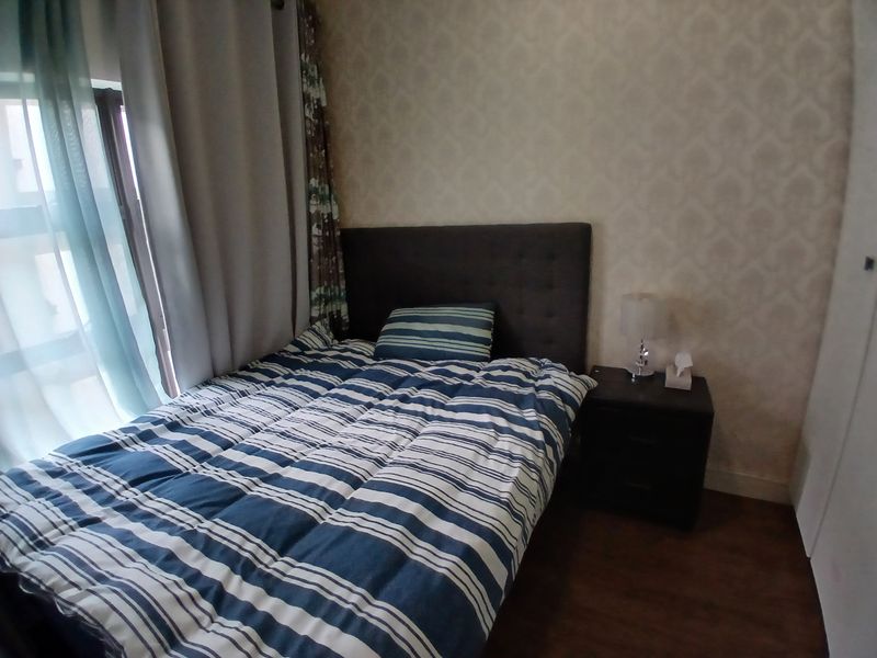 A cozy bedroom featuring laminate flooring, a built-in wardrobe, and large windows with curtains, providing a comfortable and functional living space.