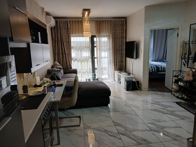 Open-plan living area featuring modern marble-look floor tiles, a compact kitchen with built-in appliances, and direct access to a balcony through sliding glass doors.