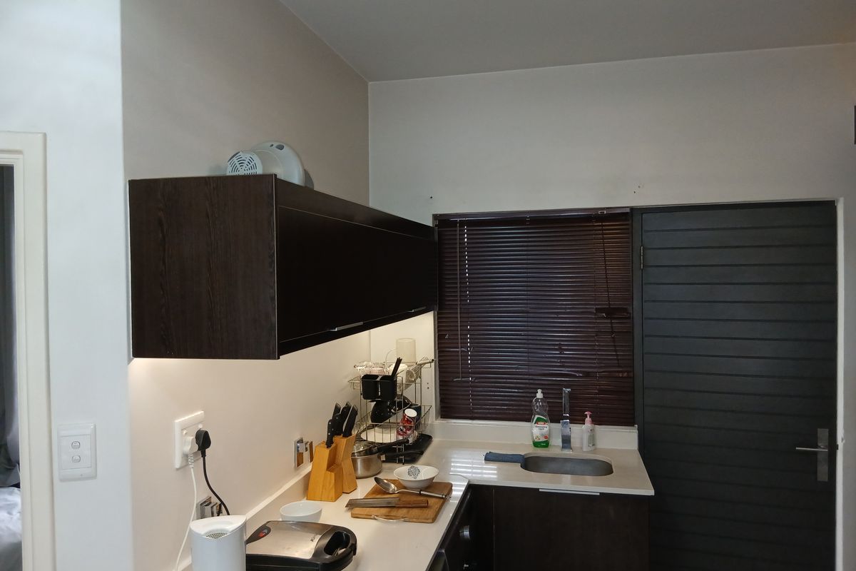 A compact kitchen area featuring dark wood cabinetry, stone countertops, an undermount sink with chrome mixer tap, and under-cabinet lighting.