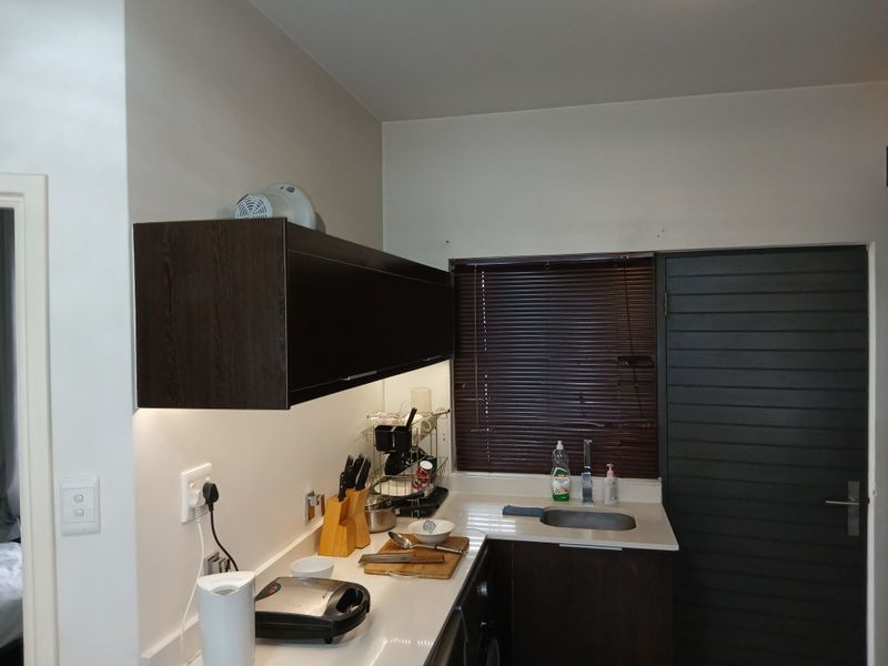 A compact kitchen area featuring dark wood cabinetry, stone countertops, an undermount sink with chrome mixer tap, and under-cabinet lighting.