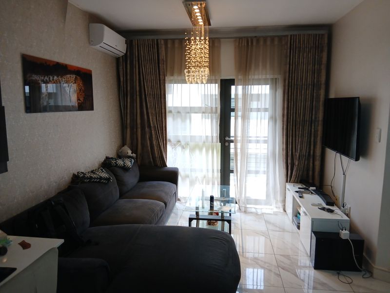 A well-maintained living room featuring polished tiled flooring, a modern crystal chandelier, and a split-system air conditioner with access to a balcony.