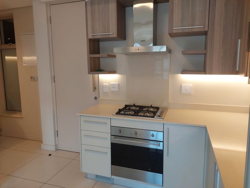 Modern kitchen featuring sleek cabinetry, stone countertops, integrated gas hob, built-in oven, and stainless steel extractor fan with under-cabinet lighting.
