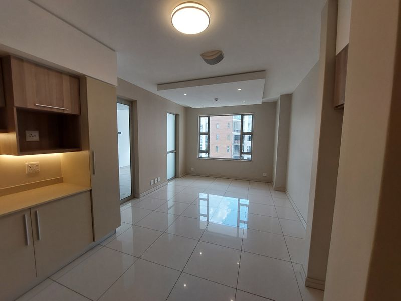 A bright, modern open-plan living area featuring sleek built-in cabinetry, polished tiled flooring, and recessed ceiling lighting, offering a clean and contemporary space.