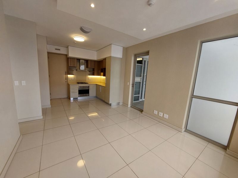 Modern open-plan living area featuring tiled floors, recessed lighting, and a compact kitchen equipped with a built-in oven, hob, and extractor fan.