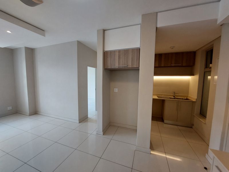 An open-plan living area featuring neutral tiled flooring, recessed lighting, and a compact kitchen nook with built-in cabinetry and under-cabinet lighting.
