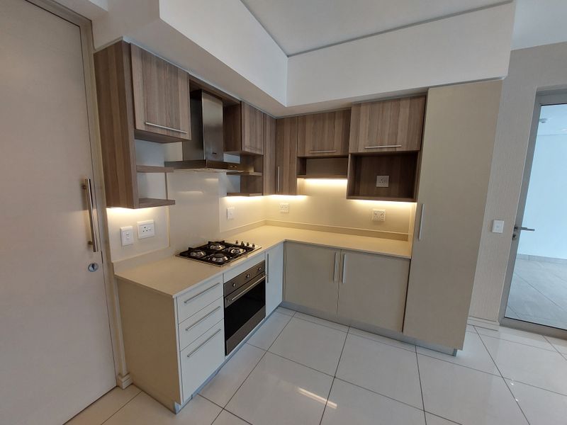 Modern kitchen featuring sleek built-in cabinetry, stone countertops, integrated gas hob, oven, and extractor fan with ambient under-cabinet lighting.