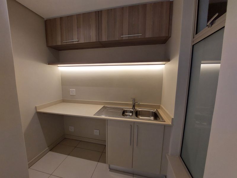 A clean and modern scullery area featuring built-in cabinetry, a stainless steel sink, and integrated under-cabinet lighting.