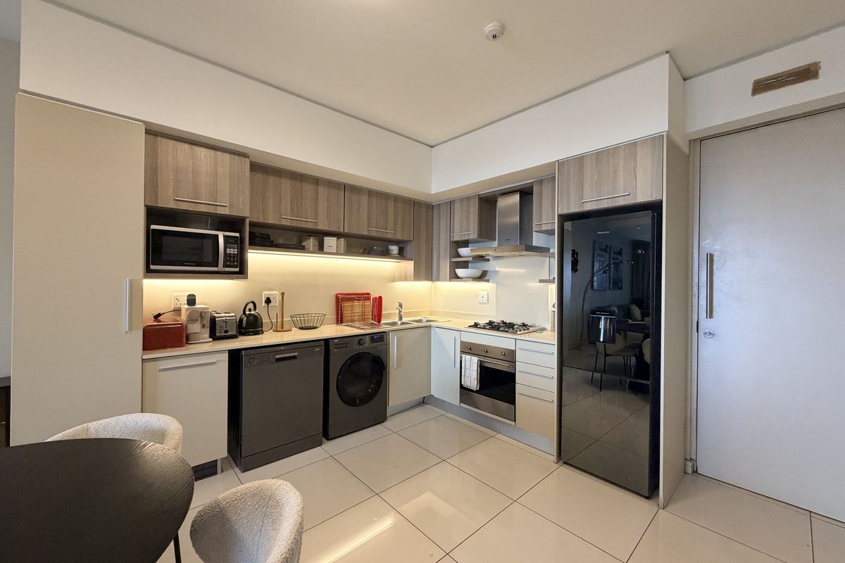 Modern kitchen featuring sleek wood-finish cabinetry, integrated appliances including an oven and hob, under-cabinet lighting, and polished floor tiles.
