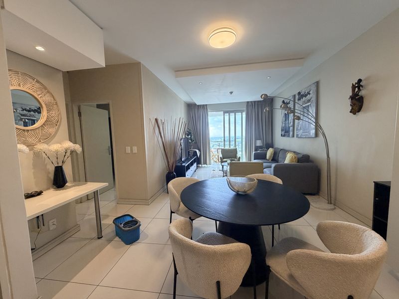 Spacious open-plan living and dining area featuring large format floor tiles, recessed ceiling lighting, and direct access to a balcony through sliding glass doors.