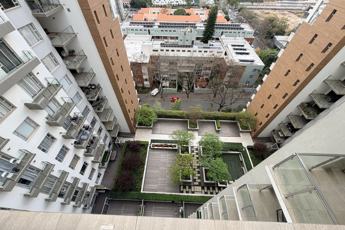 High-angle aerial view of an apartment complex featuring a central landscaped courtyard, paved walkways, and multiple private balconies with glass balustrades.