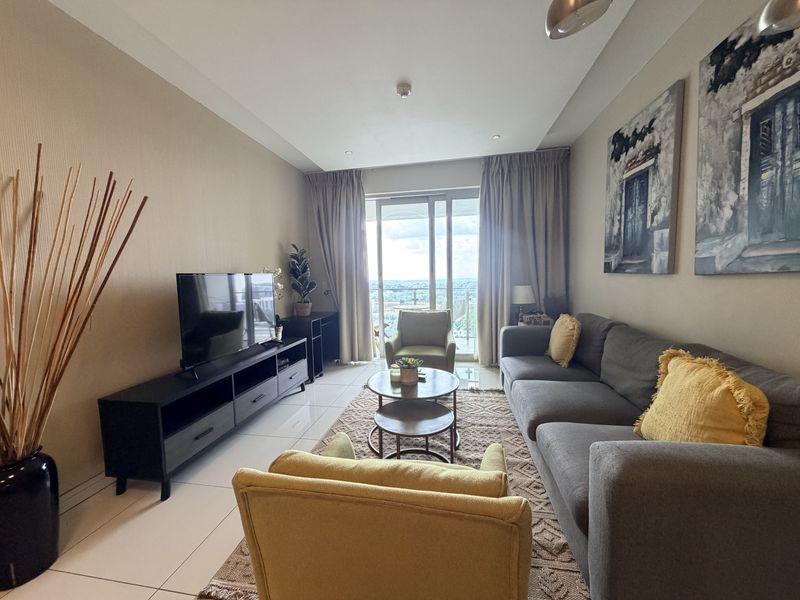 A well-maintained living room featuring tiled flooring, recessed lighting, and a large sliding glass door providing access to a balcony with natural light.