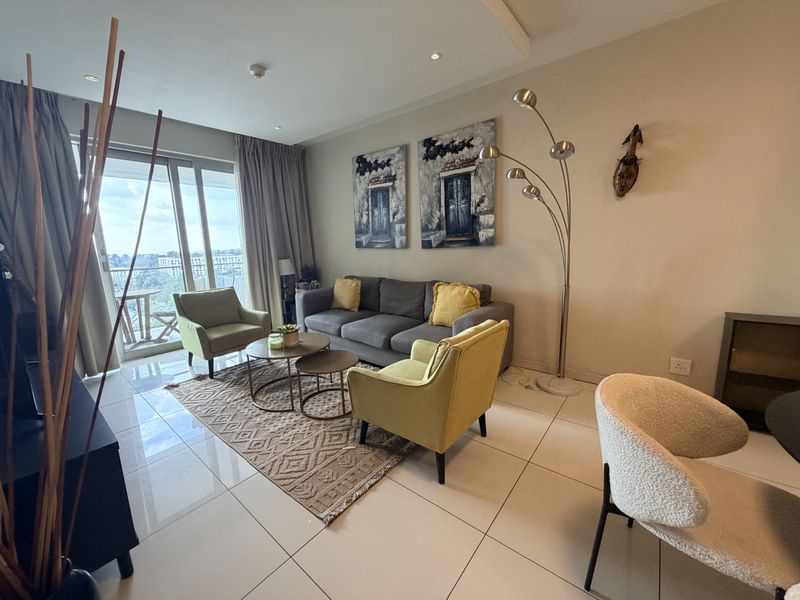 A bright and modern living room featuring large format floor tiles, recessed ceiling lighting, and a sliding glass door leading to a private balcony.