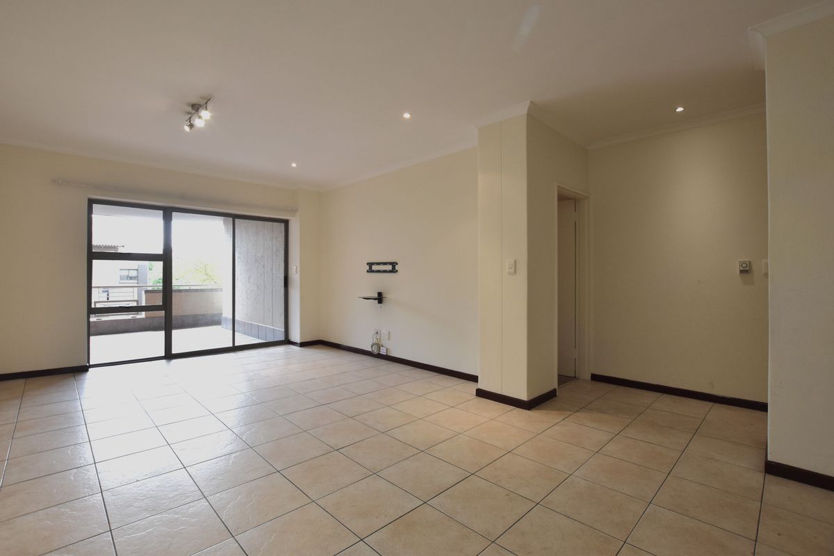 A spacious, empty living room featuring neutral tiled flooring, recessed lighting, and a large sliding glass door providing access to an outdoor balcony area.