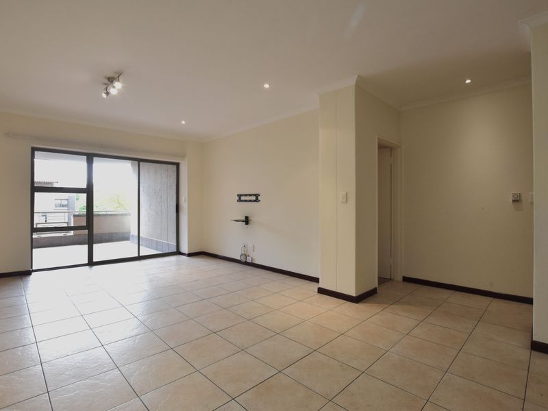 A spacious, empty living room featuring neutral tiled flooring, recessed lighting, and a large sliding glass door providing access to an outdoor balcony area.