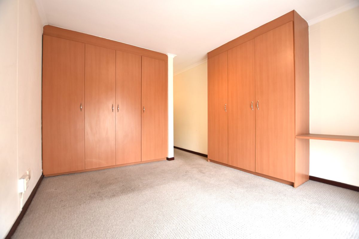A vacant bedroom featuring extensive built-in wooden cupboards and a fitted desk area, finished with neutral wall tones and carpeted flooring.