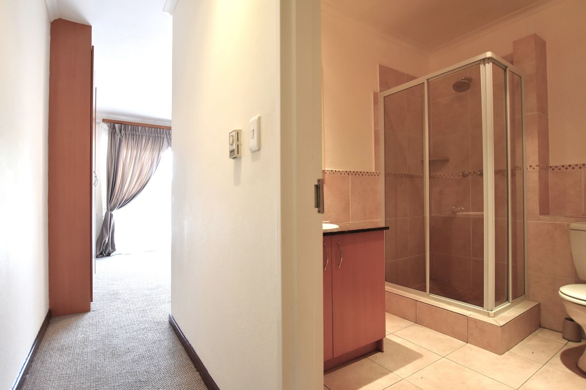 A functional bathroom featuring a shower enclosure, vanity cabinet, and toilet, adjacent to a carpeted hallway area.
