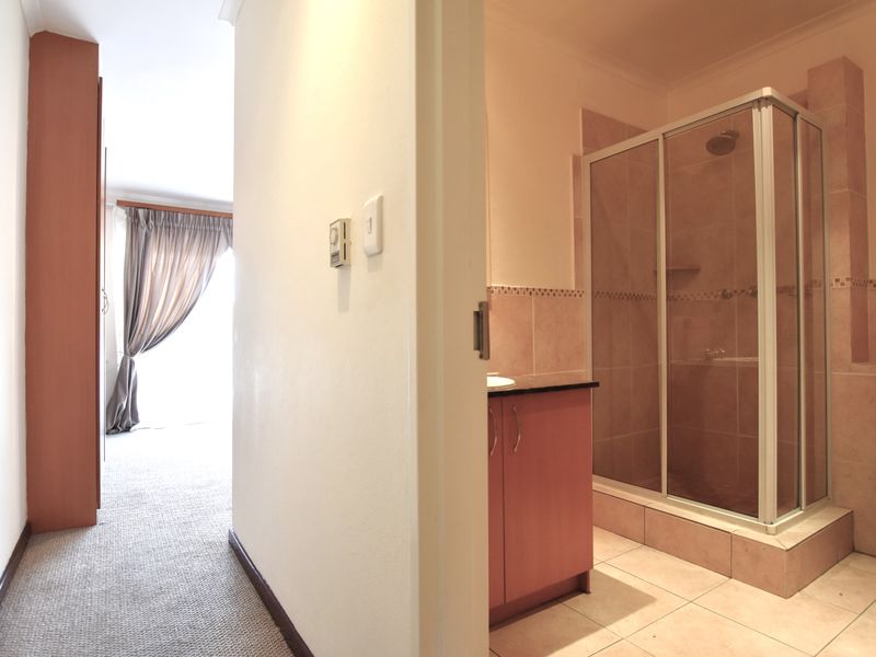 A functional bathroom featuring a shower enclosure, vanity cabinet, and toilet, adjacent to a carpeted hallway area.