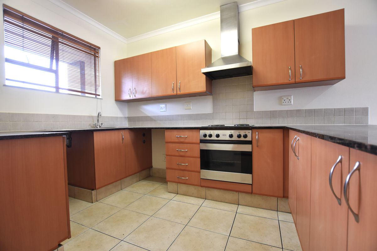 A functional kitchen featuring laminate cabinetry, granite countertops, a built-in oven with extractor fan, and tiled flooring.