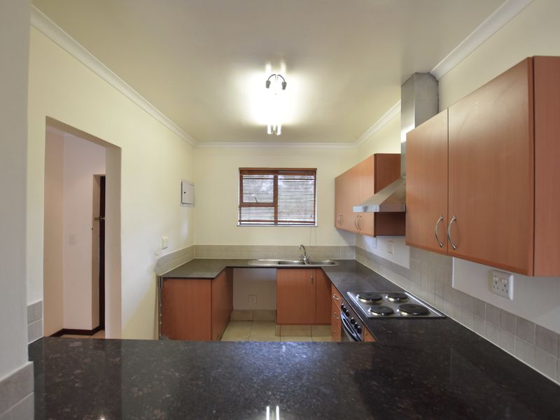 A functional kitchen featuring laminate cabinetry, granite countertops, an electric hob with extractor fan, and a tiled backsplash.
