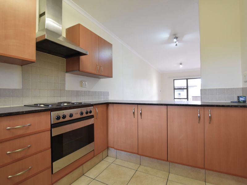 A functional kitchen featuring laminate cabinetry, granite countertops, a built-in oven with extractor fan, and neutral ceramic floor tiles.