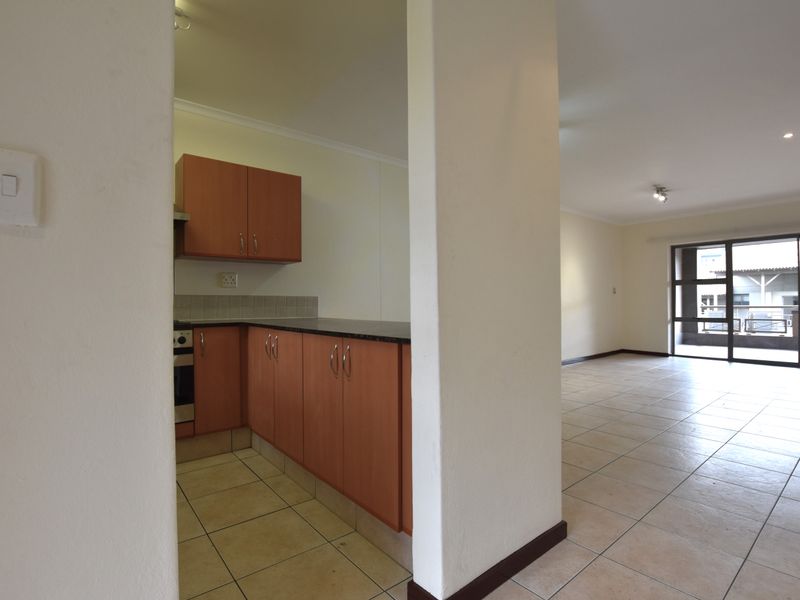 An open-plan living area featuring a compact kitchen with built-in cabinetry and tiled flooring, leading to a bright space with sliding glass doors.