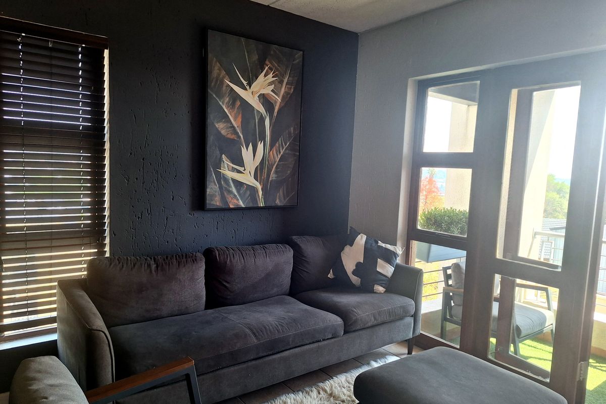 A modern living room featuring a dark textured accent wall, large glass doors providing natural light, and direct access to an outdoor balcony area.