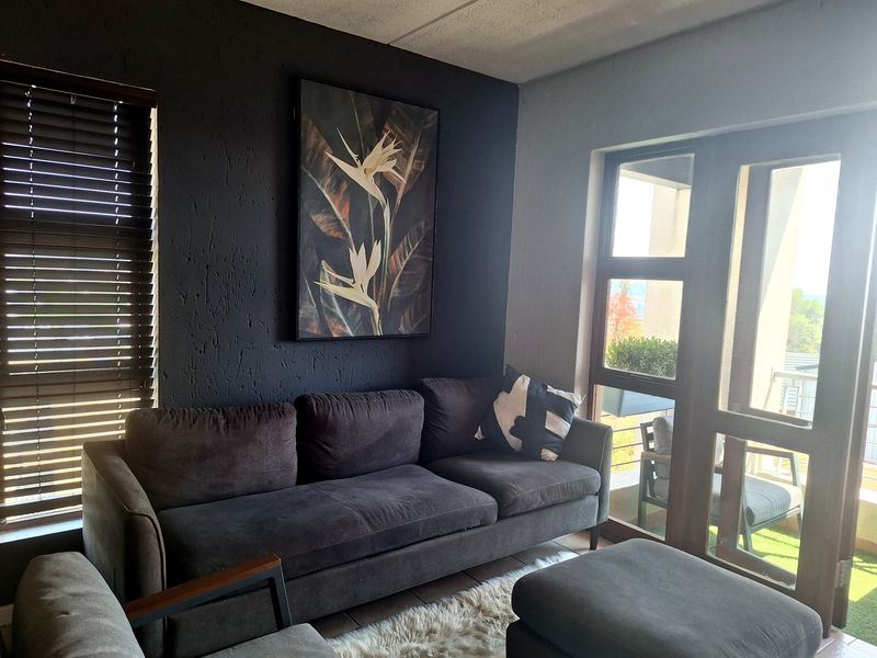 A modern living room featuring a dark textured accent wall, large glass doors providing natural light, and direct access to an outdoor balcony area.