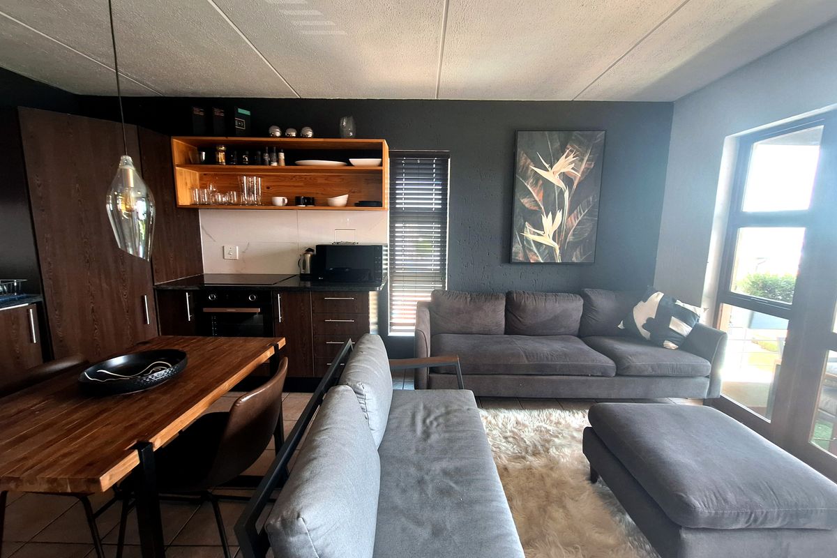 Modern open-plan living area featuring a compact kitchen with dark cabinetry, integrated oven, and a seamless transition to the lounge space.