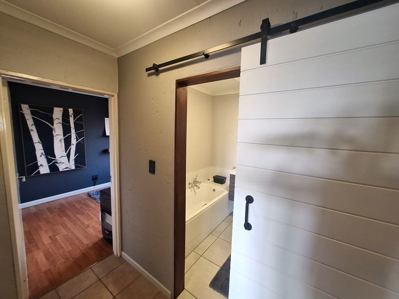 Hallway featuring a modern sliding barn door providing access to a bathroom with a built-in bathtub and tiled flooring.
