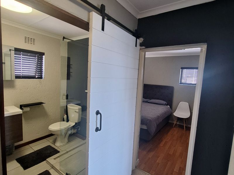 A modern bathroom featuring a sliding barn door, glass-enclosed shower, and vanity, with an adjacent view into a bedroom area.