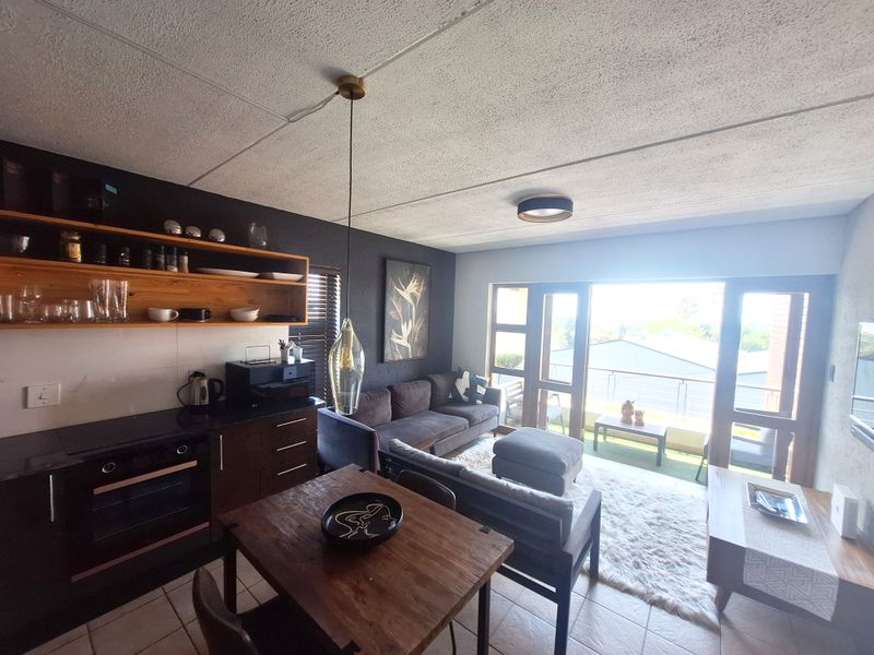 Open-plan living and kitchen area featuring dark cabinetry, built-in oven, wooden shelving, and large sliding doors leading to a balcony with outdoor views.