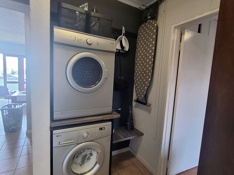 A compact laundry nook featuring a stacked washing machine and tumble dryer with built-in shelving and tiled flooring.