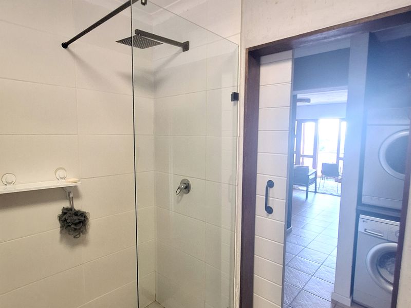 Modern bathroom featuring a walk-in shower with a glass screen and rain shower head, adjacent to a laundry area with a sliding door.